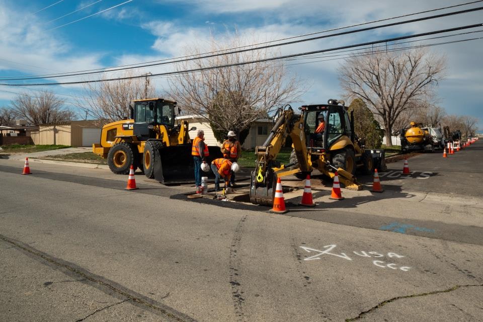 Construction workers repairing a street with heavy machinery and traffic cones.