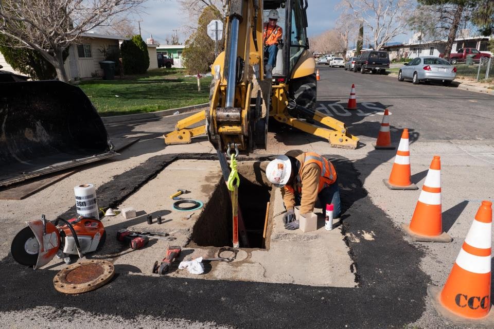 Construction workers repairing a street with orange cones, tools, and machinery.