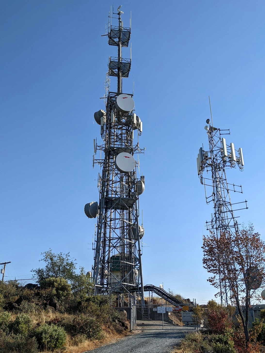 Two large communication towers with multiple antennas against a clear blue sky.