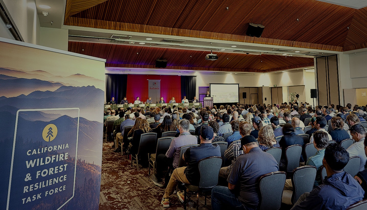 A conference with attendees, a panel discussion, and a sign for the California Wildfire & Forest Resilience Task Force.