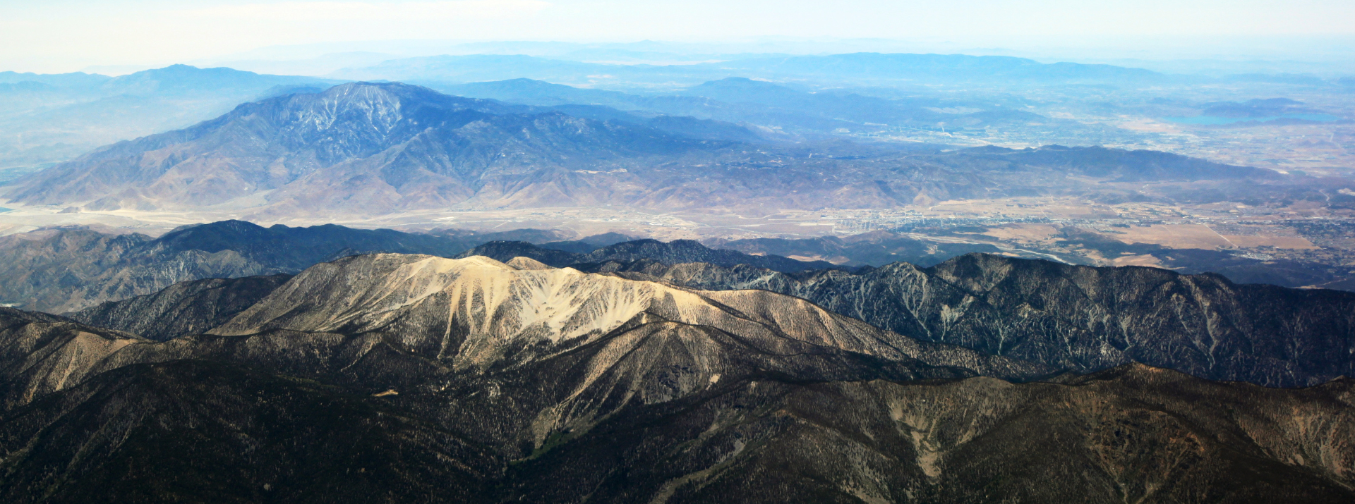 Aerial view of layered mountain ranges and valleys extending into the distance under a clear sky.