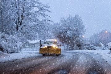 Snow Plow truck on street at dawn or dusk with snow all around and trees