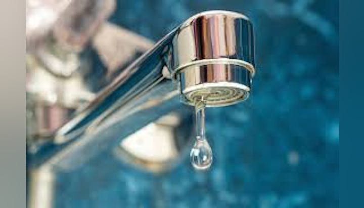 A water droplet hanging from a shiny tap with a blurred blue background.