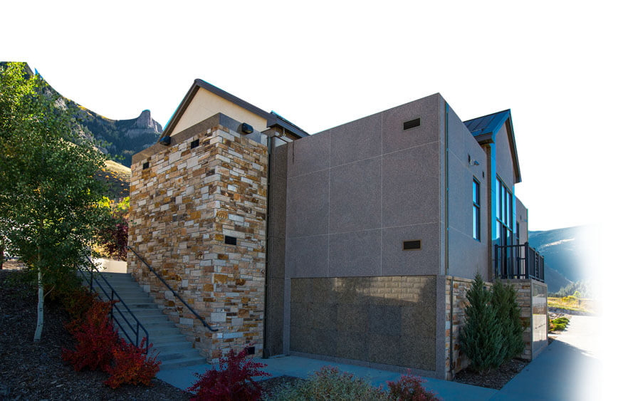 Modern building with stone and concrete facade, stairs, and trees, set against a mountainous background.