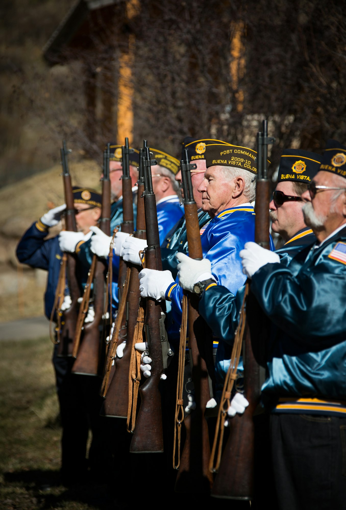 A group of veterans in uniform hold rifles in a ceremonial formation.