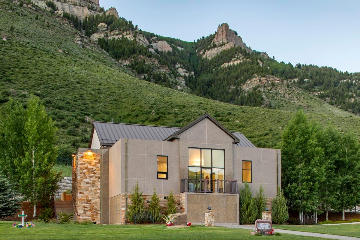 Modern house with large windows, nestled in lush green hills and surrounded by trees.