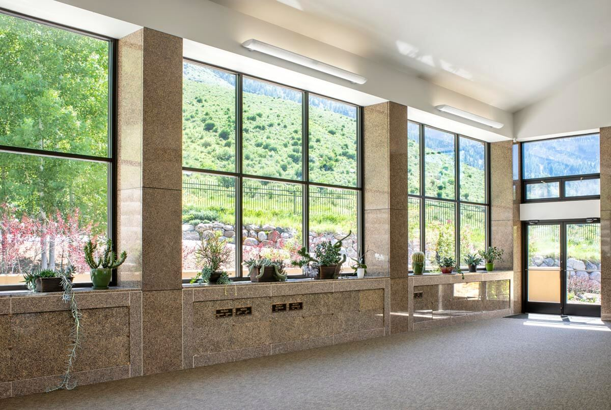 A bright room with large windows, potted plants on the sill, and an outdoor view of green hills.