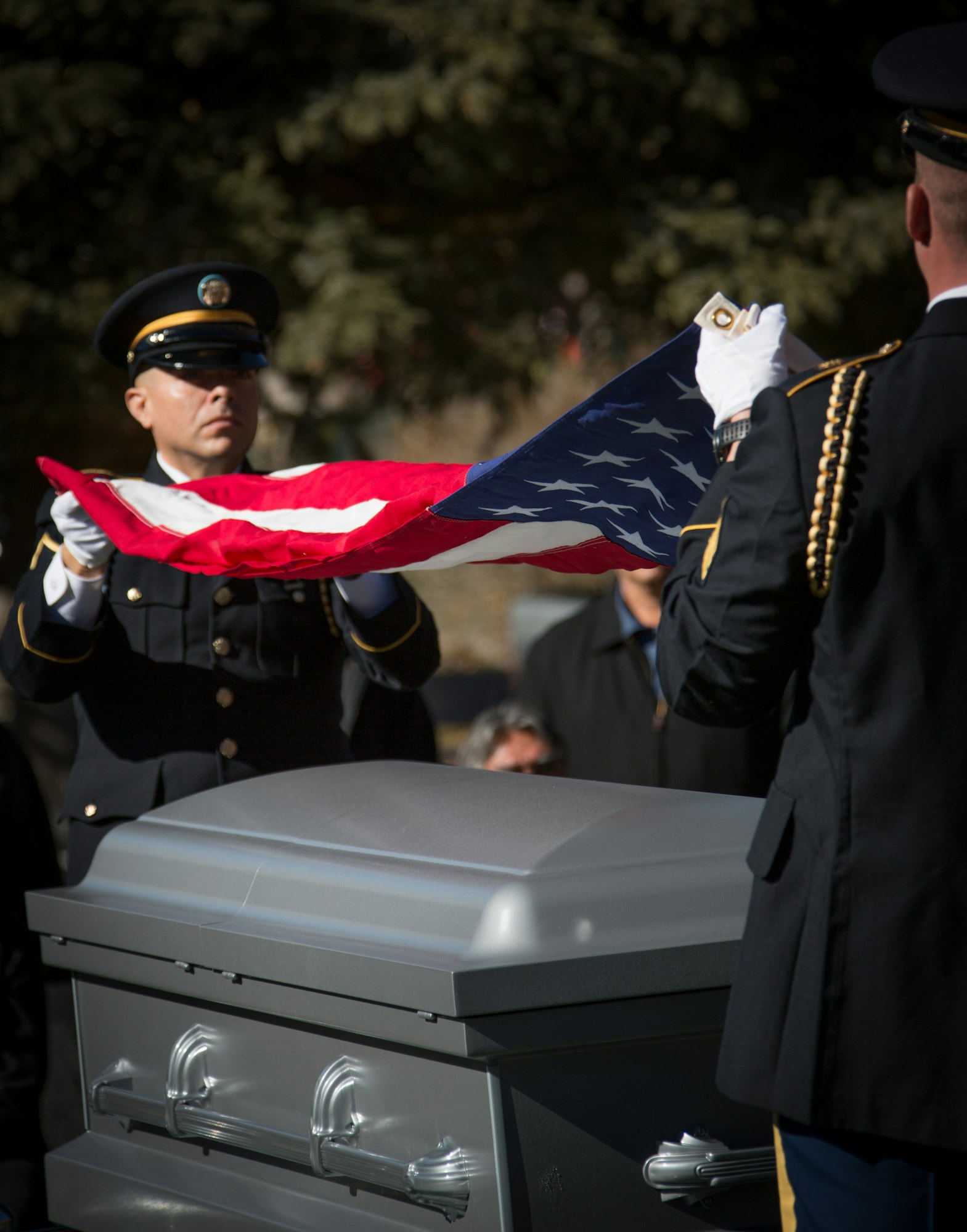 Military personnel folding a flag over a casket at a funeral ceremony.