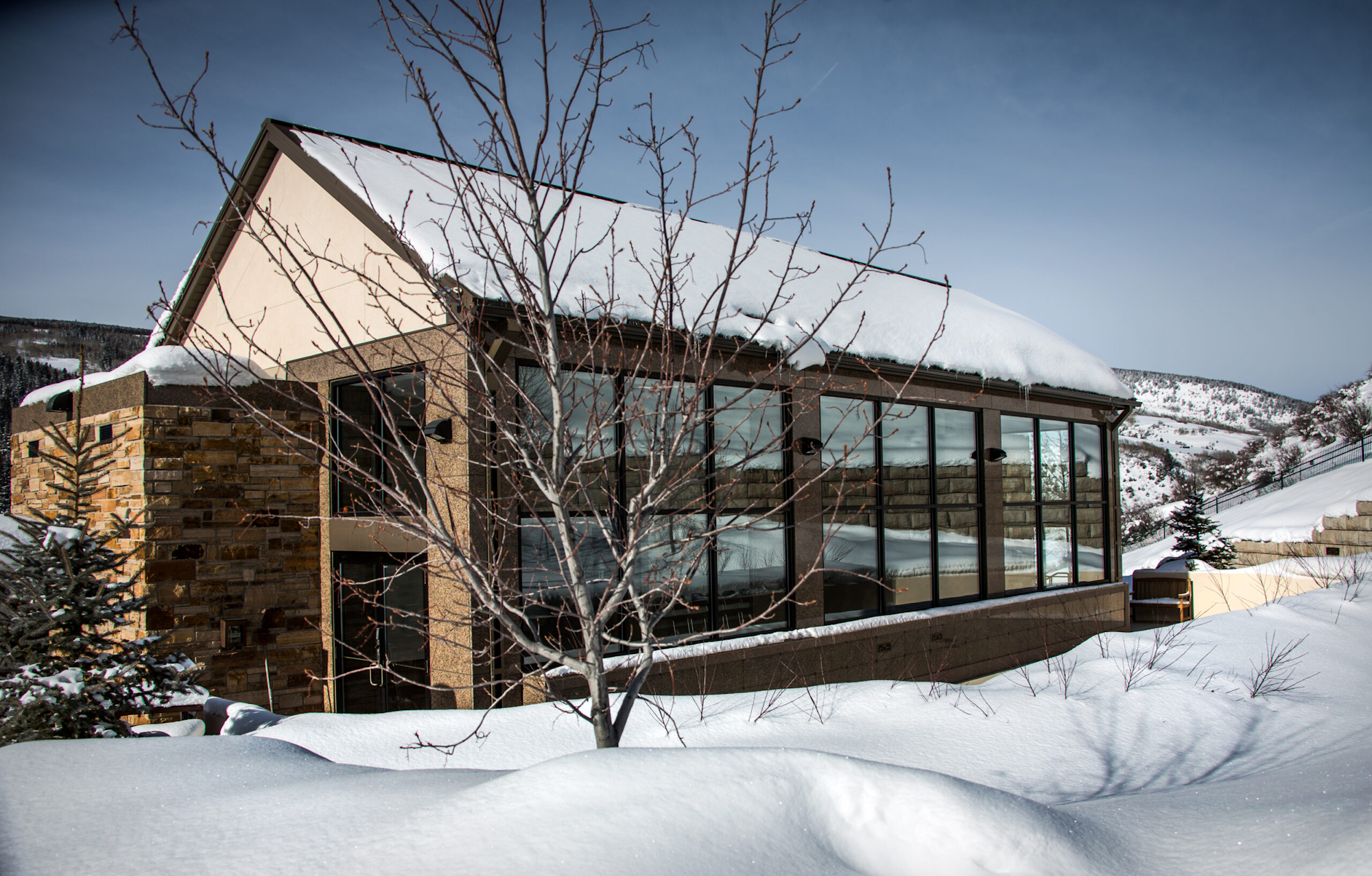 A modern house with large windows, covered in snow, set in a snowy landscape with mountains in the background.