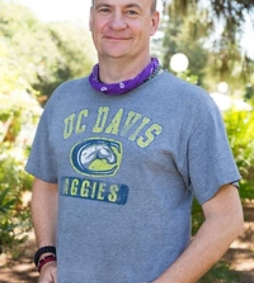 A person wearing a UC Davis Aggies t-shirt and a purple bandana standing outdoors.