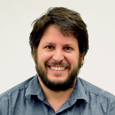 A man with dark hair and a beard, wearing a gray shirt, smiling at the camera.