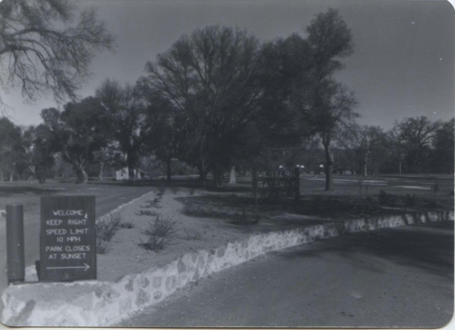A black-and-white image of the newly created park entrance with signs for "Western Gateway Park," including speed limit and closing times.