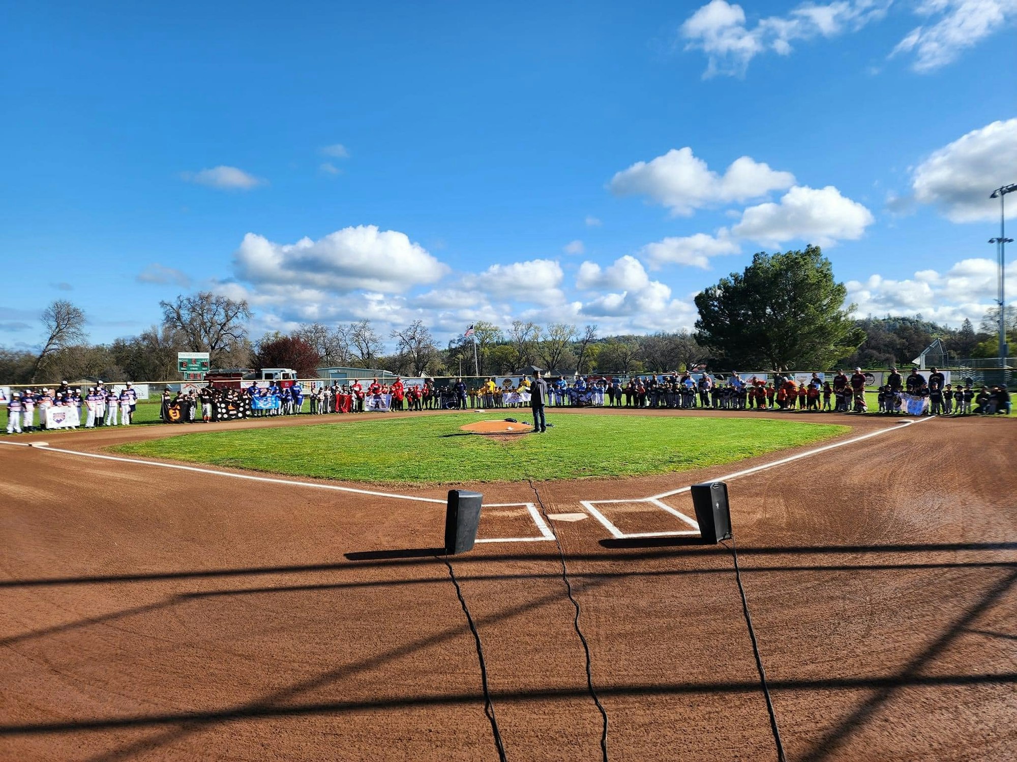 A group of people in team uniforms stands in a baseball field, forming a semicircle.