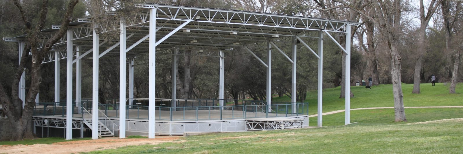Outdoor stage or pavilion in a park, surrounded by trees and grassy area.