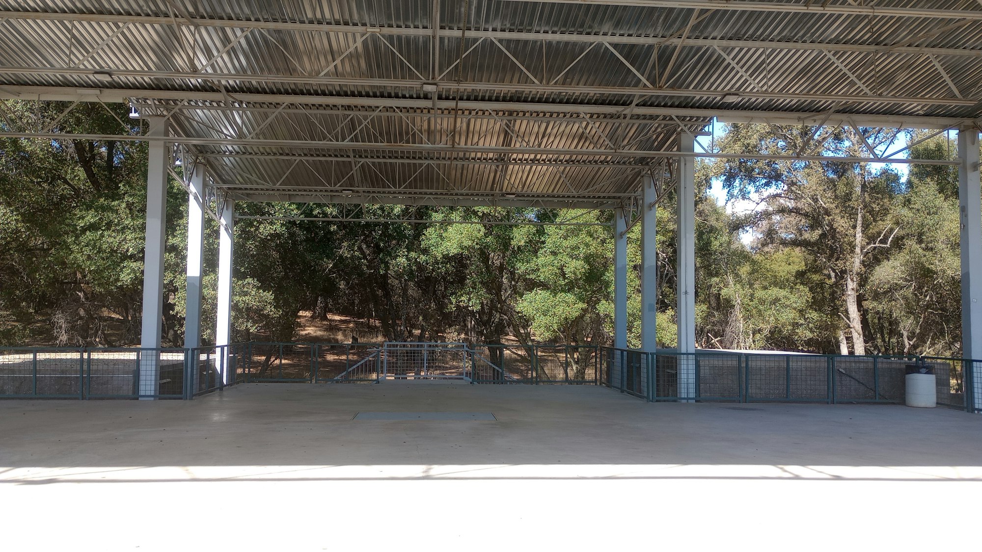Covered outdoor platform with metal roof and railings, surrounded by trees.