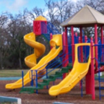A colorful playground with slides, climbing structures, and a small roof, set outdoors with trees in the background.