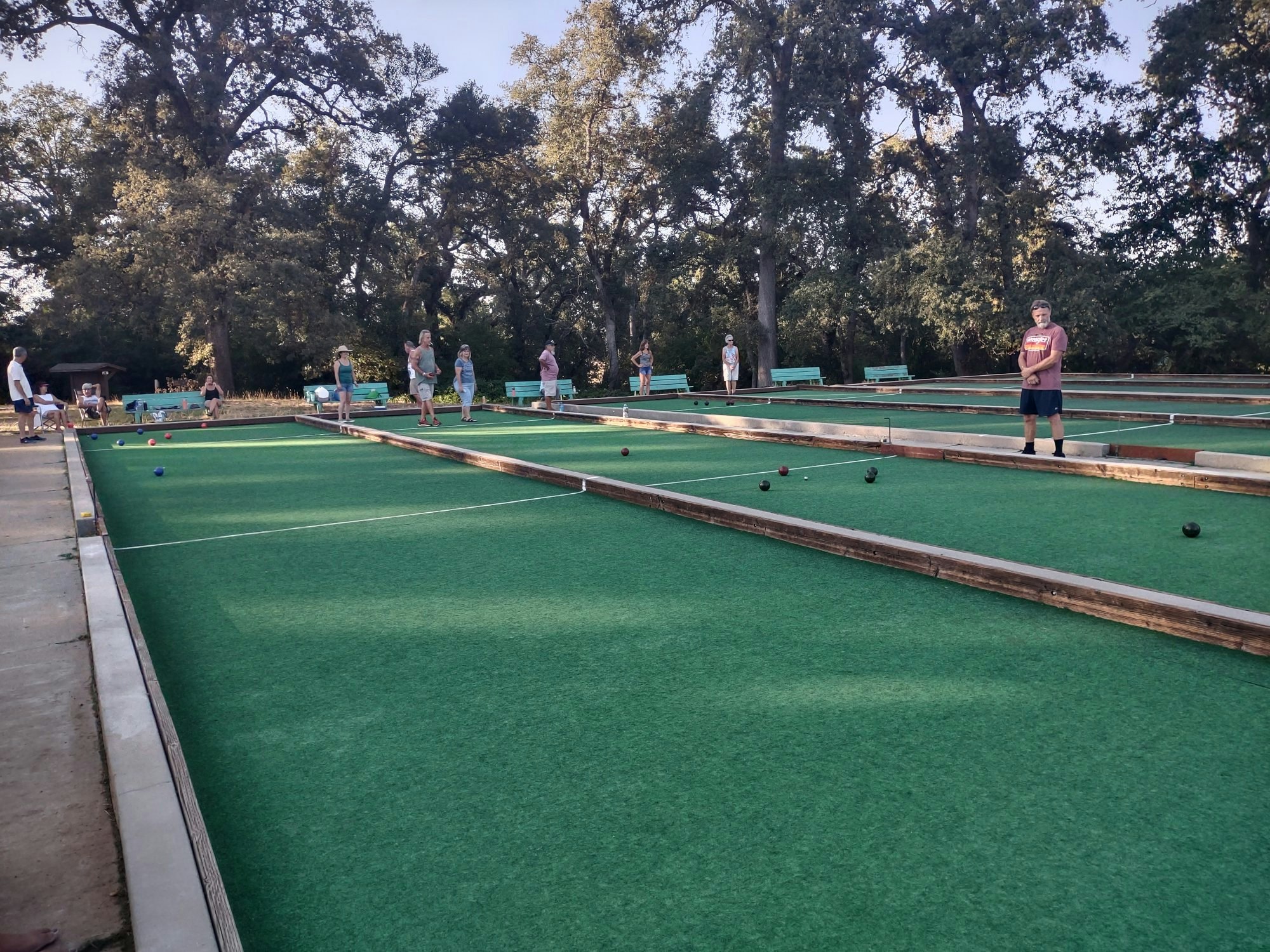 People playing bocce on outdoor courts surrounded by trees.
