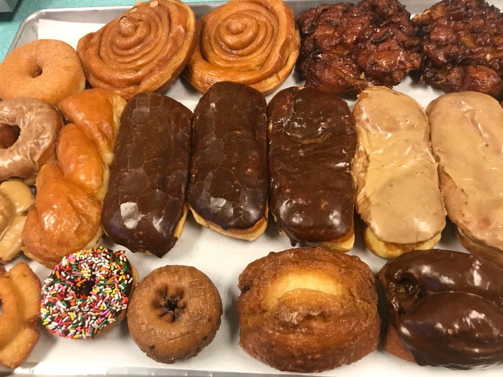 A variety of donuts and pastries, including cinnamon rolls, chocolate eclairs, sprinkle donuts, and fritters on a tray.