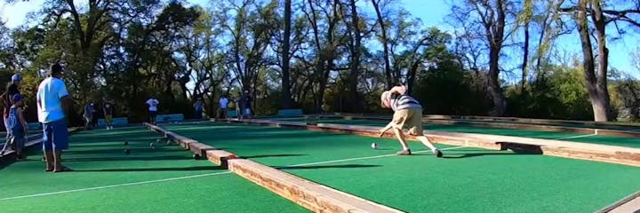 People playing bocce ball on a court surrounded by trees.