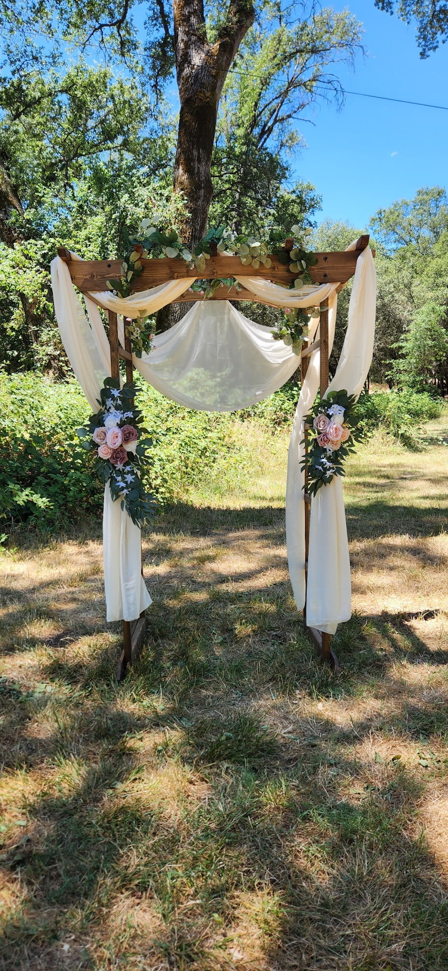 Wooden arbor with white drapery and floral decorations in the Four Creek Sites outdoor setting.