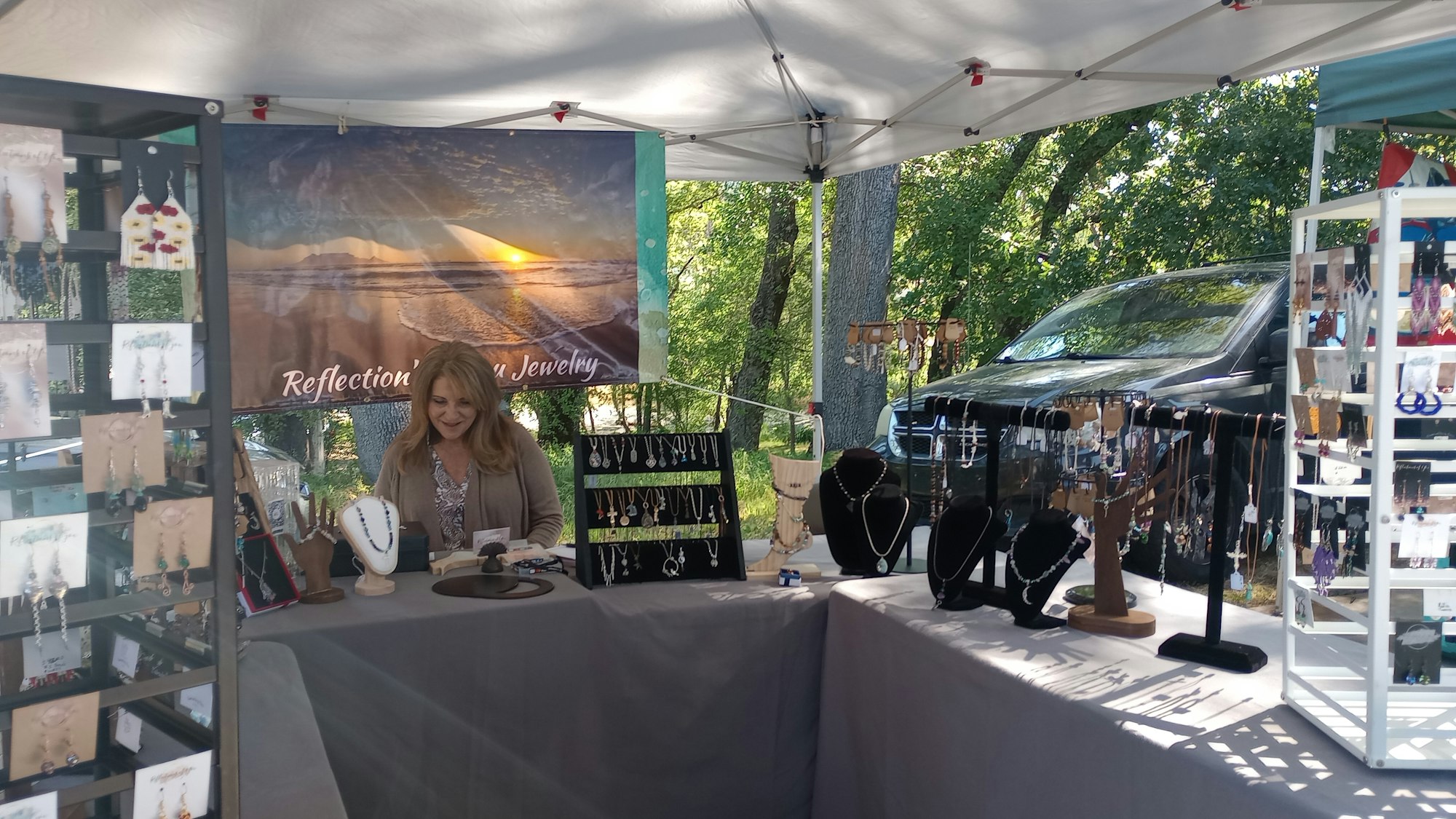 Outdoor jewelry booth with displays and a person behind the counter, surrounded by trees.