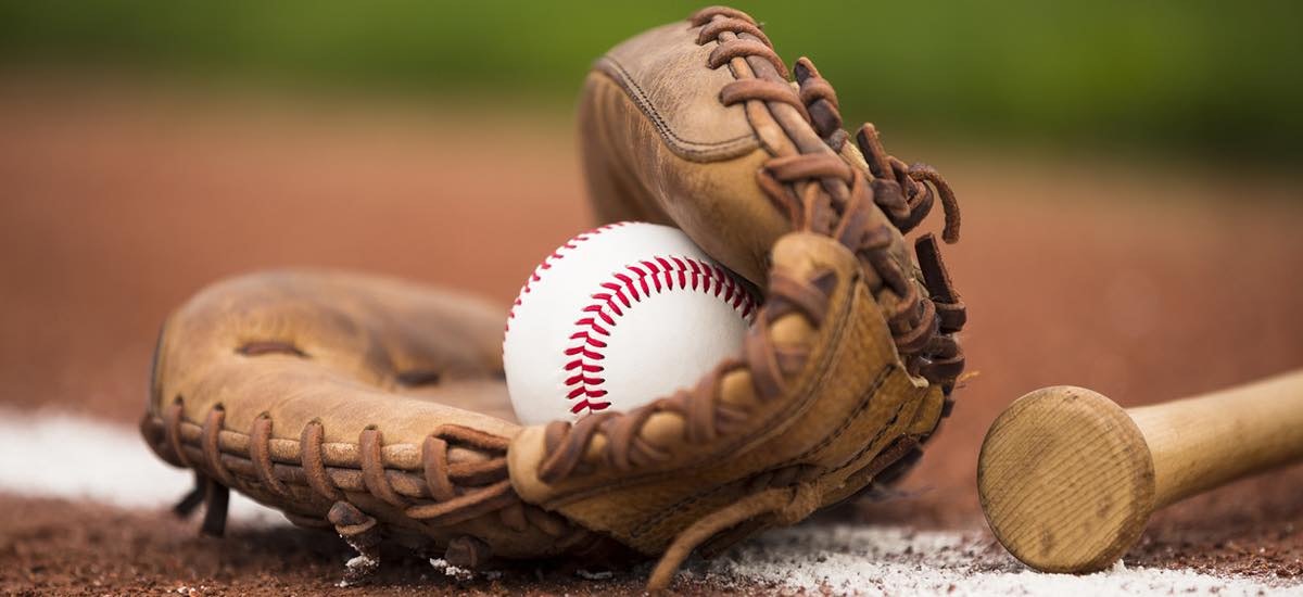 A baseball glove with a ball inside, next to a bat on a baseball field.