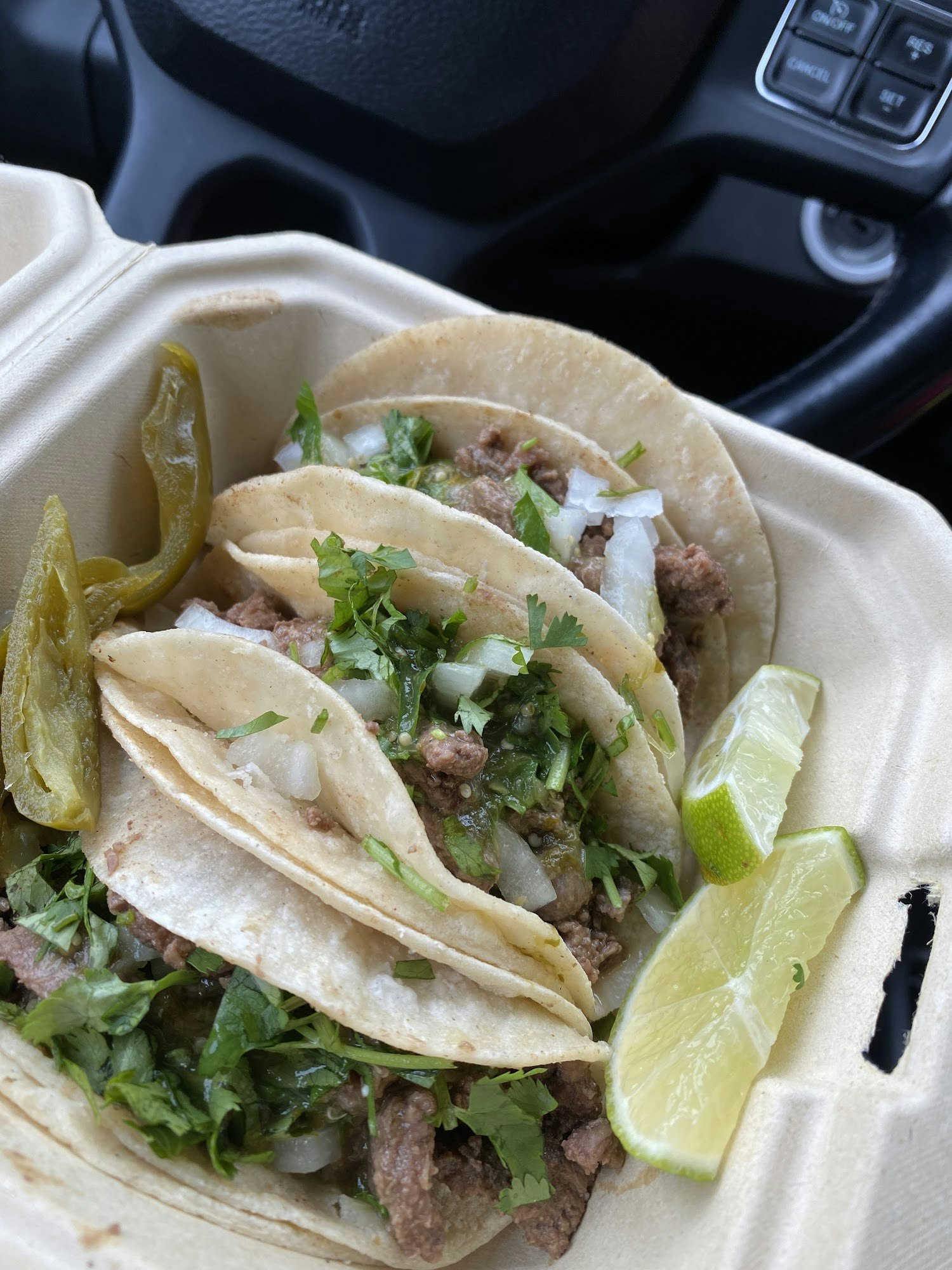 Tacos with meat, onions, and cilantro in a takeout box with lime wedges and jalapeños.