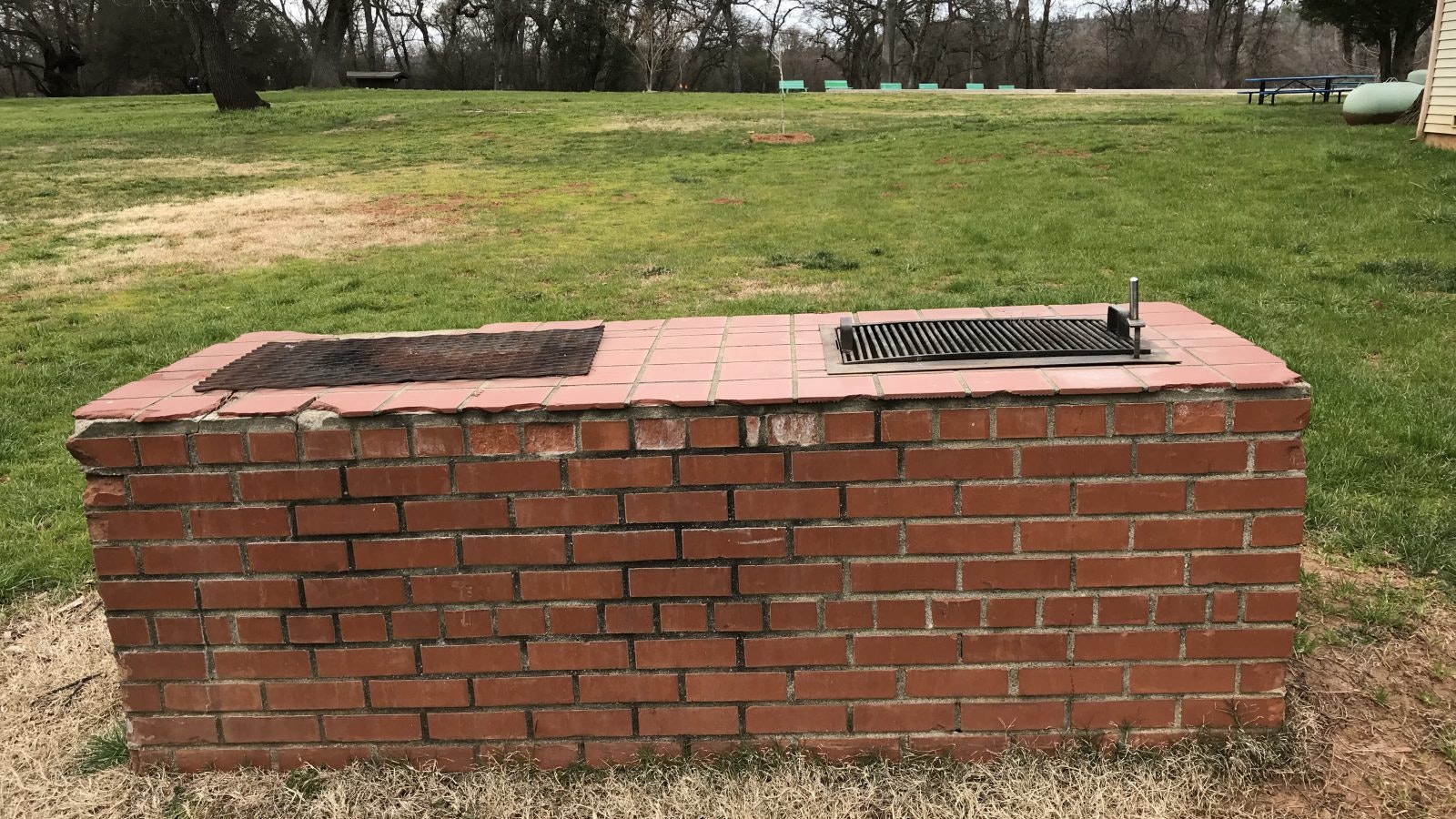 A brick outdoor grill with two metal grates, set in a grassy area.