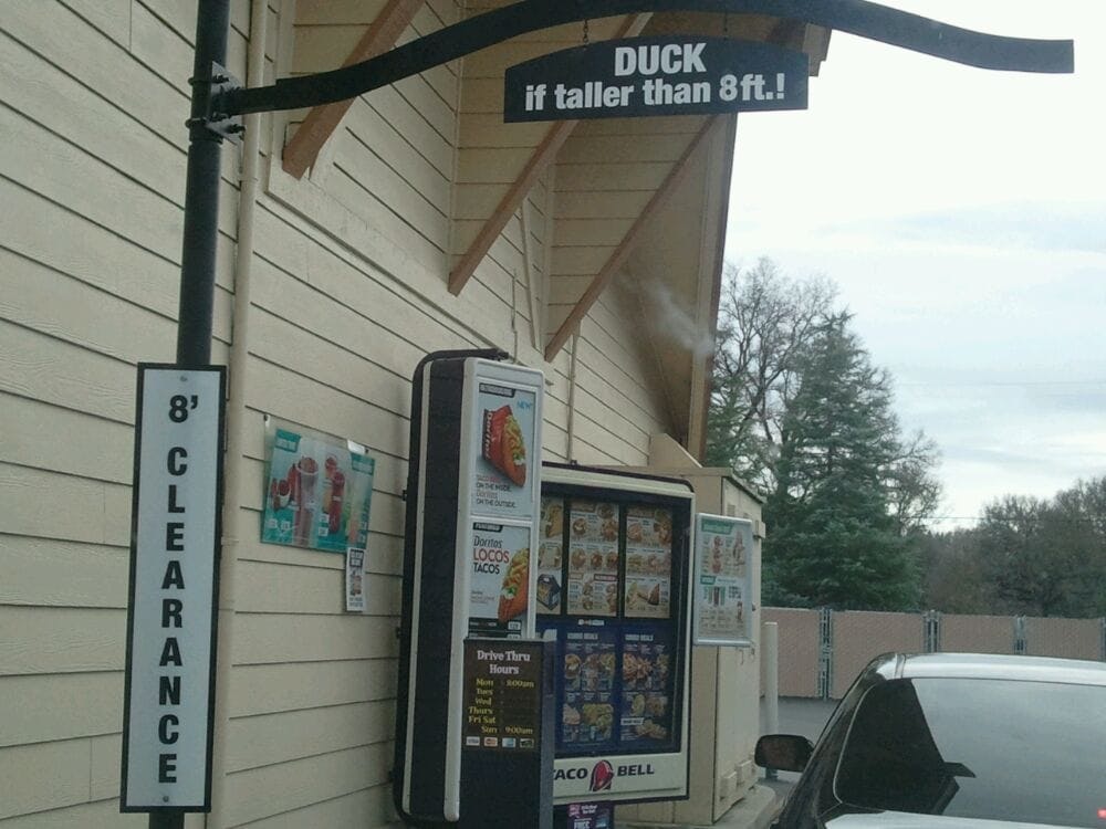 Drive-thru with a Taco Bell menu, 8' clearance sign, and a warning to duck if taller than 8 ft.
