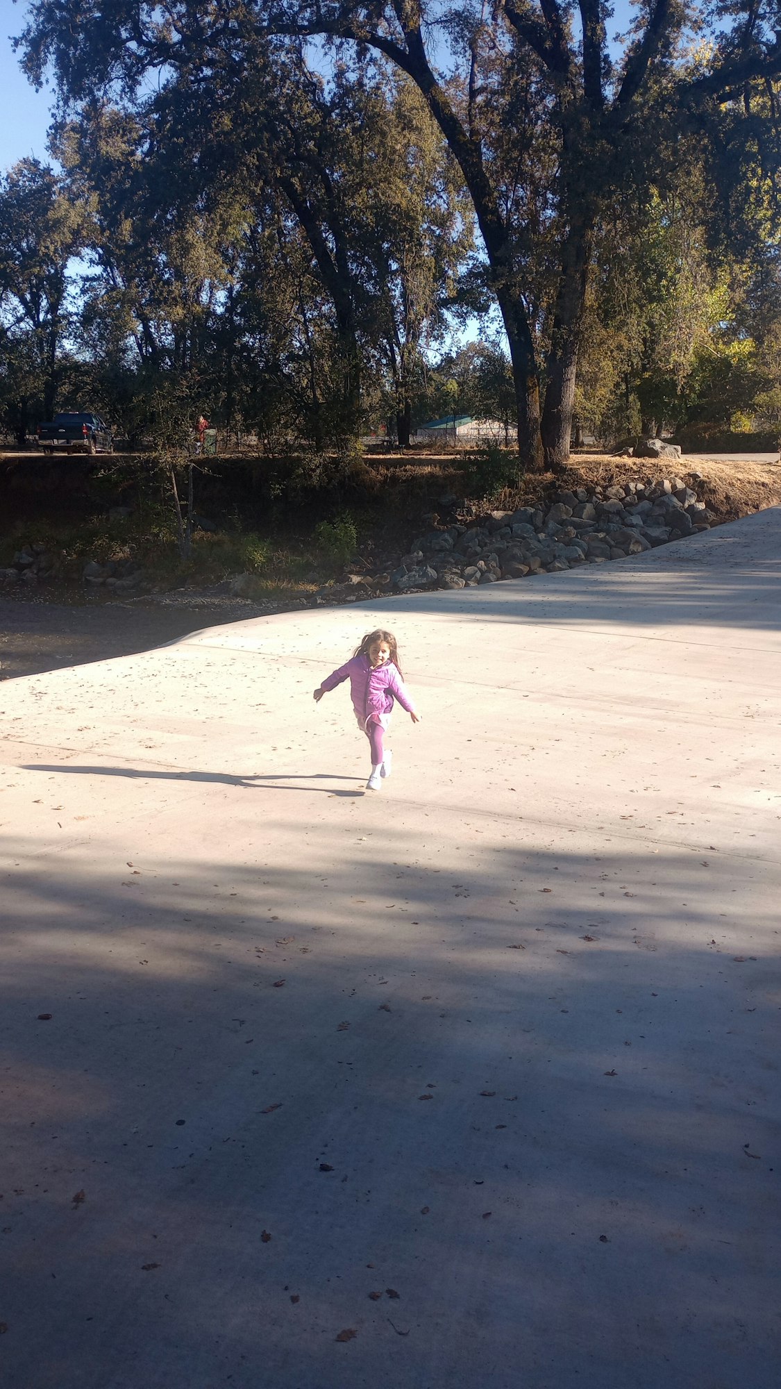 A child in pink clothes stands on a large concrete surface surrounded by trees.