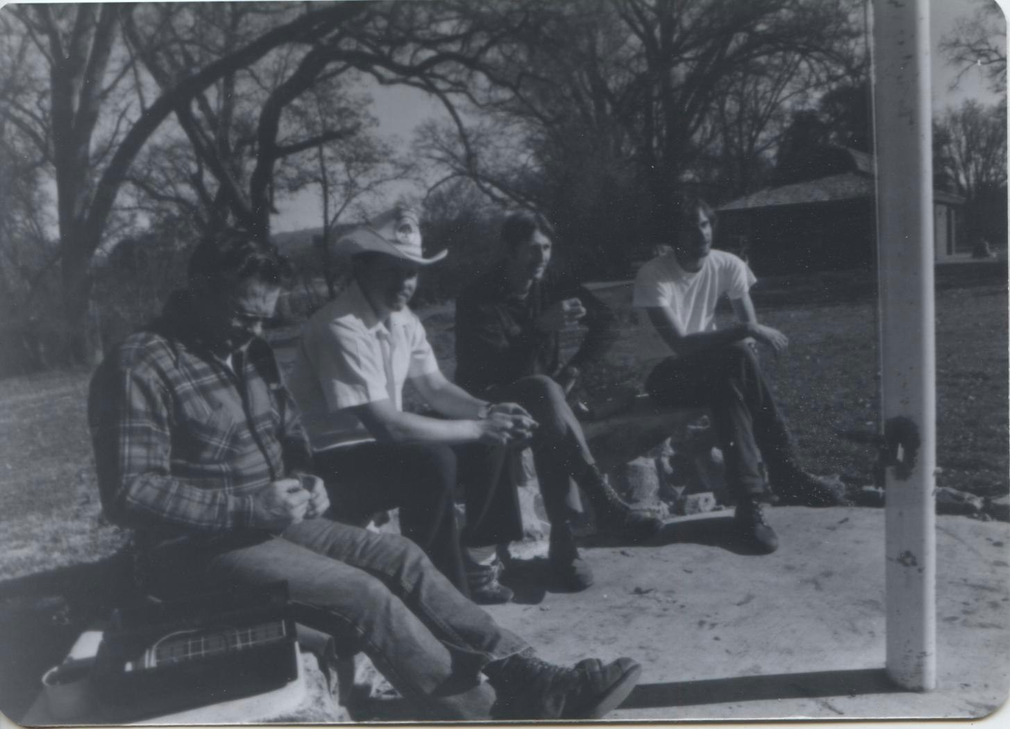 A black-and-white photo of four park volunteers sitting outdoors, engaged in conversation, with trees in the background.