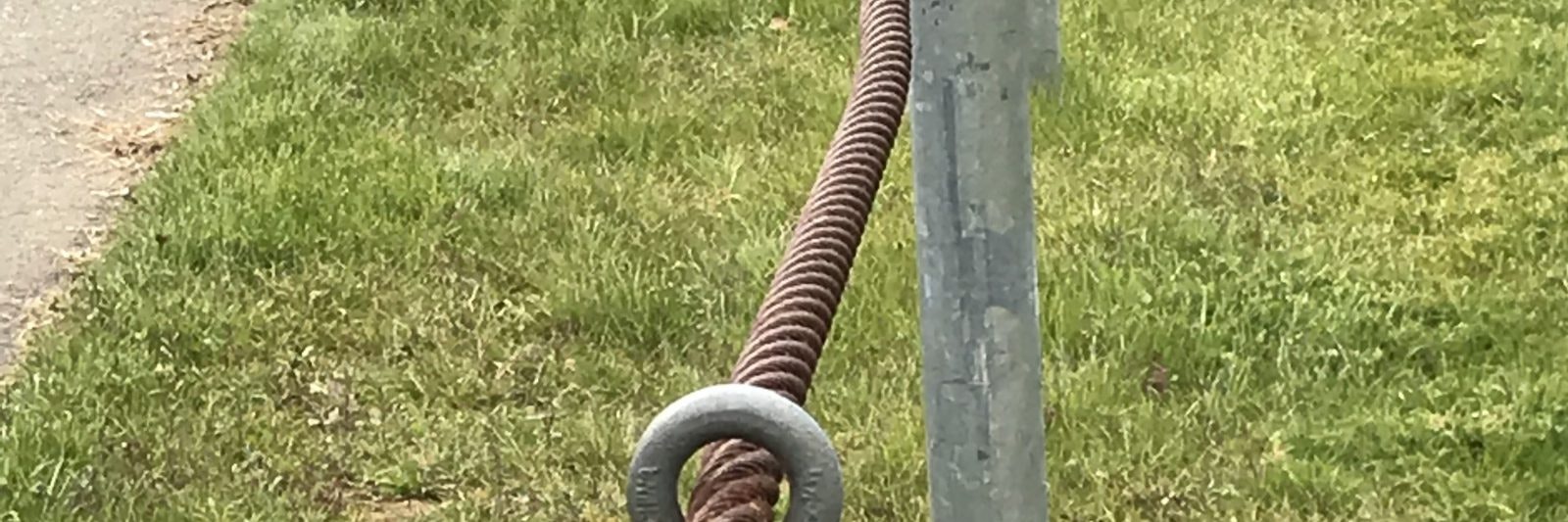 A coiled metal cable attached to a metal pole on a grassy area.