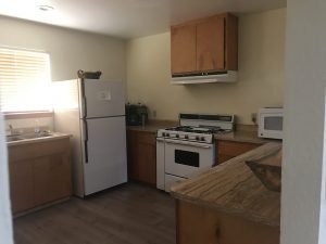 A small kitchen with a fridge, stove, microwave, wooden cabinets, and a sink under a window.
