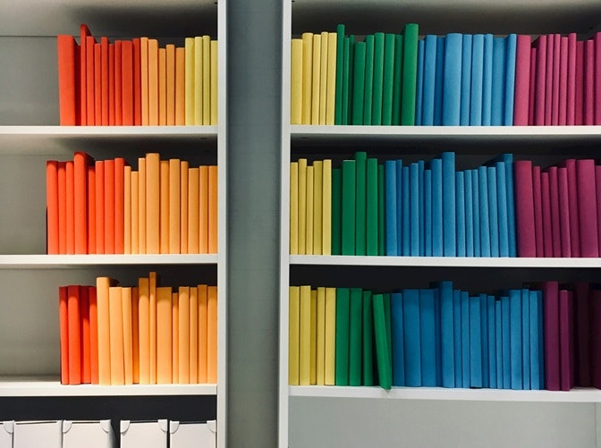 Bookshelves with colorful books arranged by hue, creating a rainbow effect.