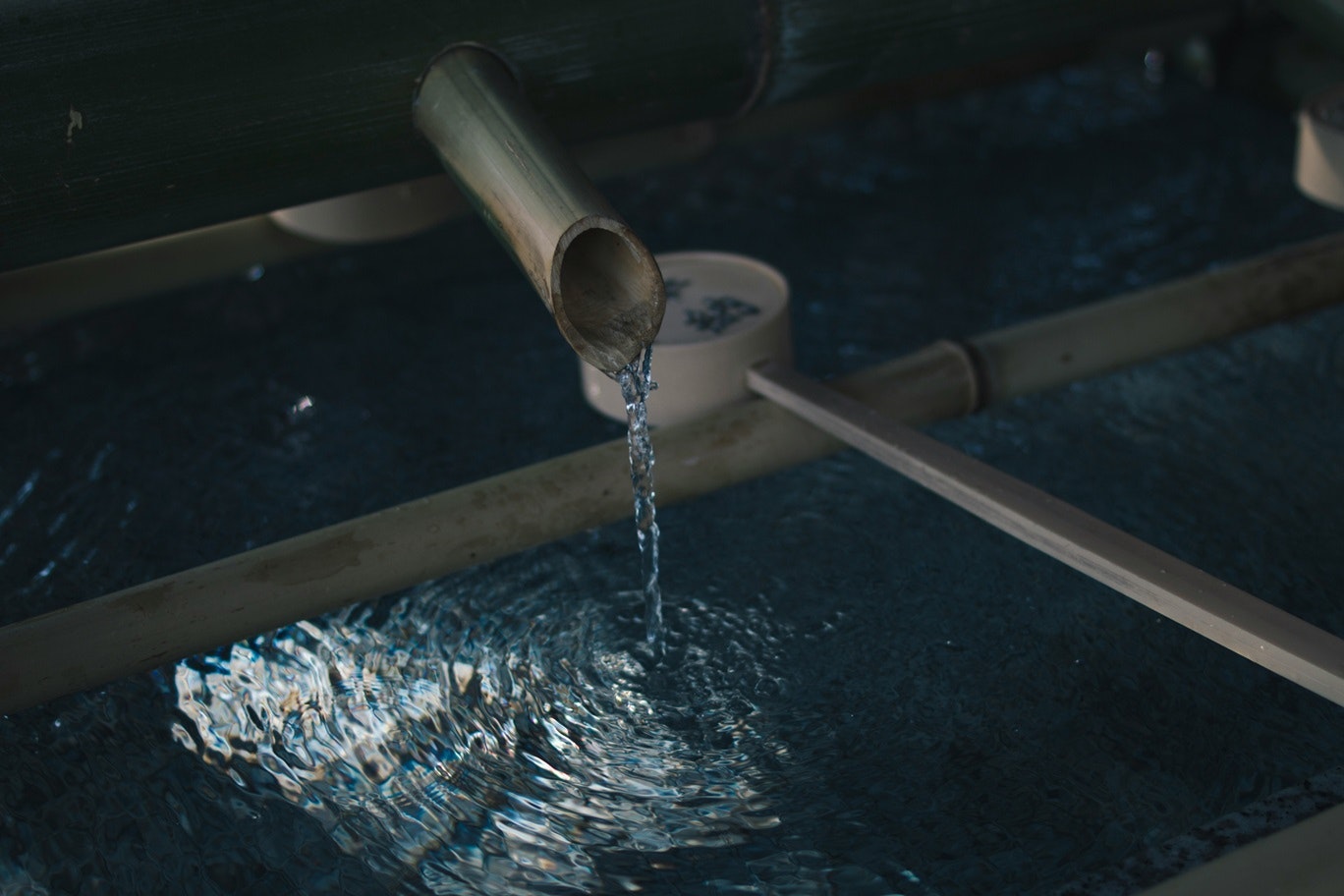 Water flowing from a bamboo pipe into a stone basin with a ladle.