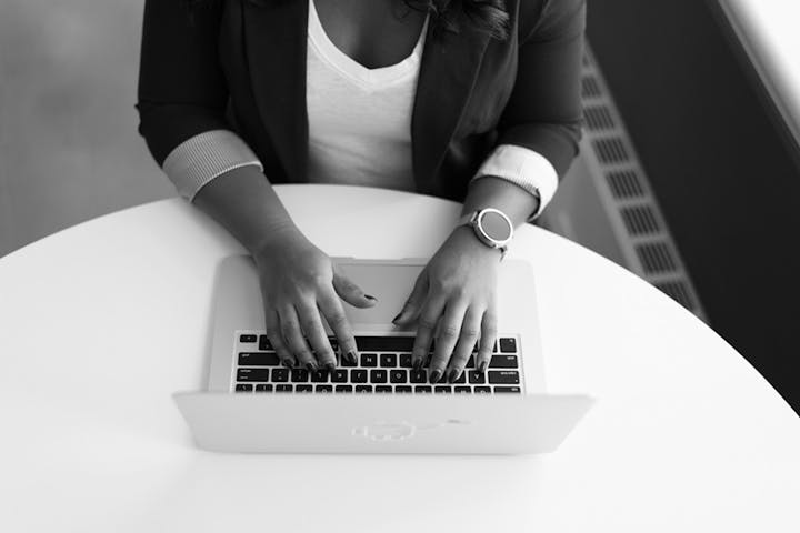 A black and white photo of a person typing on a laptop.