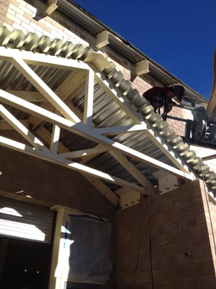 A person working on a roof structure with metal beams and a clear blue sky in the background.