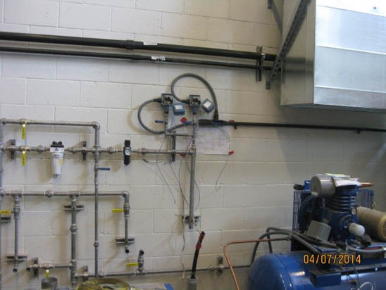 Pipes and meters on a wall with a mechanical device in a utility room.