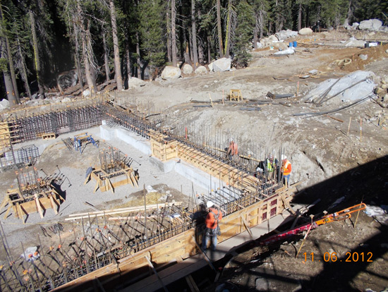 Construction site with workers, rebar, and concrete forms in a forested area.