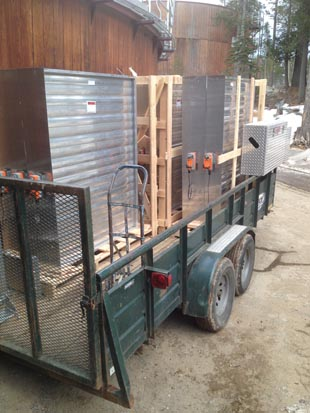 A trailer loaded with large metallic equipment secured with wooden frames, parked outdoors.