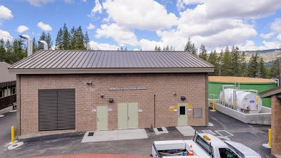 A building with a vent system, parked vehicles, and storage tanks against a cloudy sky.