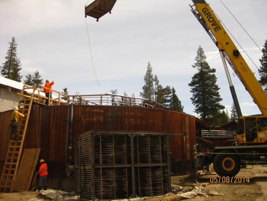 Construction site with a crane lifting materials, workers, and wooden structures.