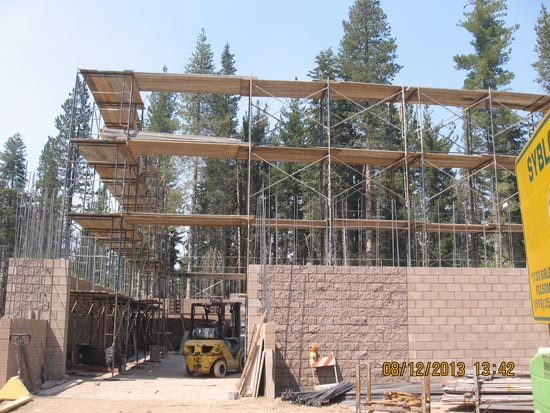 A construction site with scaffolding, brick walls, a forklift, and trees in the background.