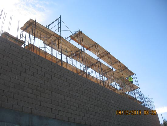 Scaffolding set up at a construction site against a brick wall with a clear blue sky.