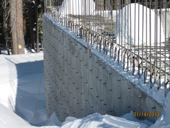 Concrete wall with rebar and hook-like attachments in a snowy setting.