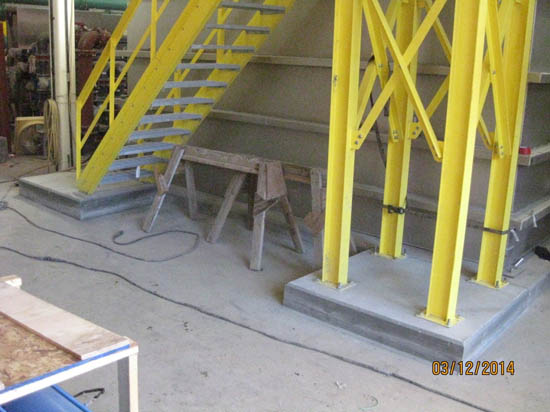 Industrial setting with yellow metal stairs and supports, a wooden sawhorse, and cables on the floor.