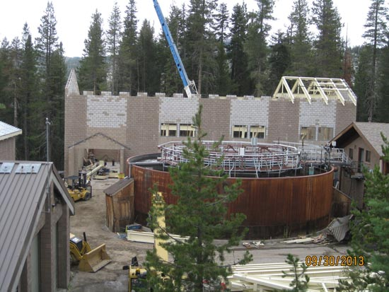 A construction site with a circular structure, scaffolding, heavy machinery, and a building in progress among trees.