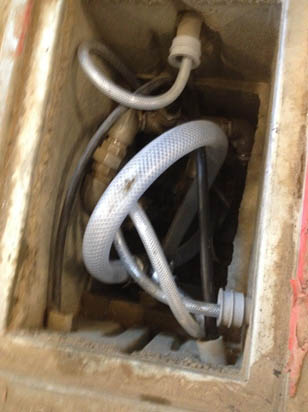 A tangled metal hose in a small concrete compartment.