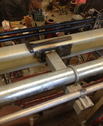 A close-up of industrial pipes and machinery, with a complex metal junction and workshop tools in the background.