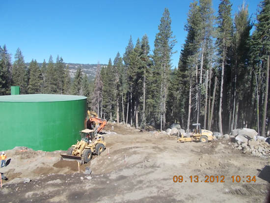 Construction site with heavy machinery near a large green tank surrounded by tall trees, dated 09.13.2012.